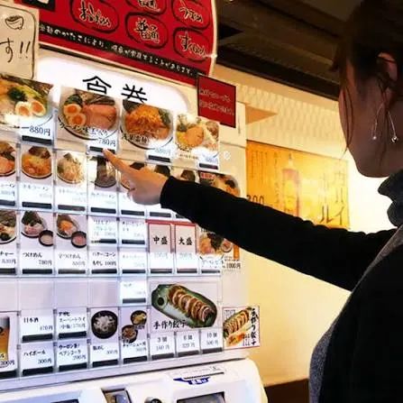 A hand pressing a button on a soba restaurant ticket machine in Tokyo.